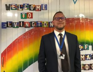 Andrew Buttery standing in front of a display with an image of a rainbow and the text 'welcome to Elvington'